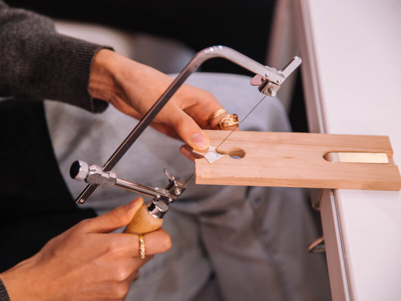 Close up of hands using a fret saw with a wooden handle at a jewellery workbench